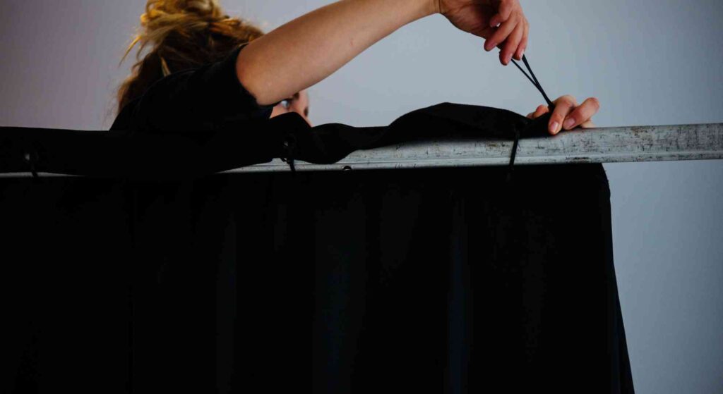 A female event stylist fixing black draping to a pipe at an event venue.