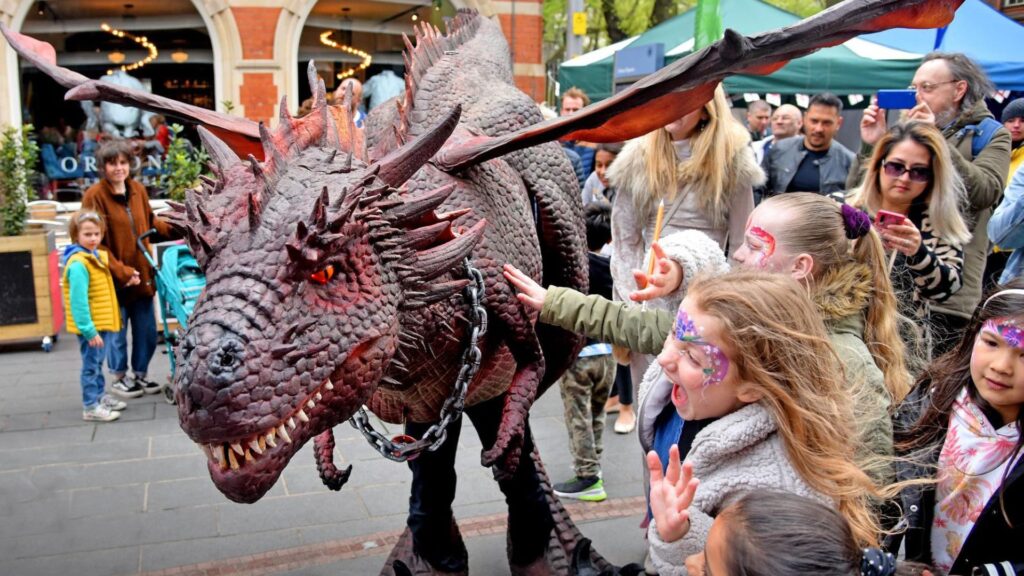 People are petting a medieval themed life-size puppet dragon in the street