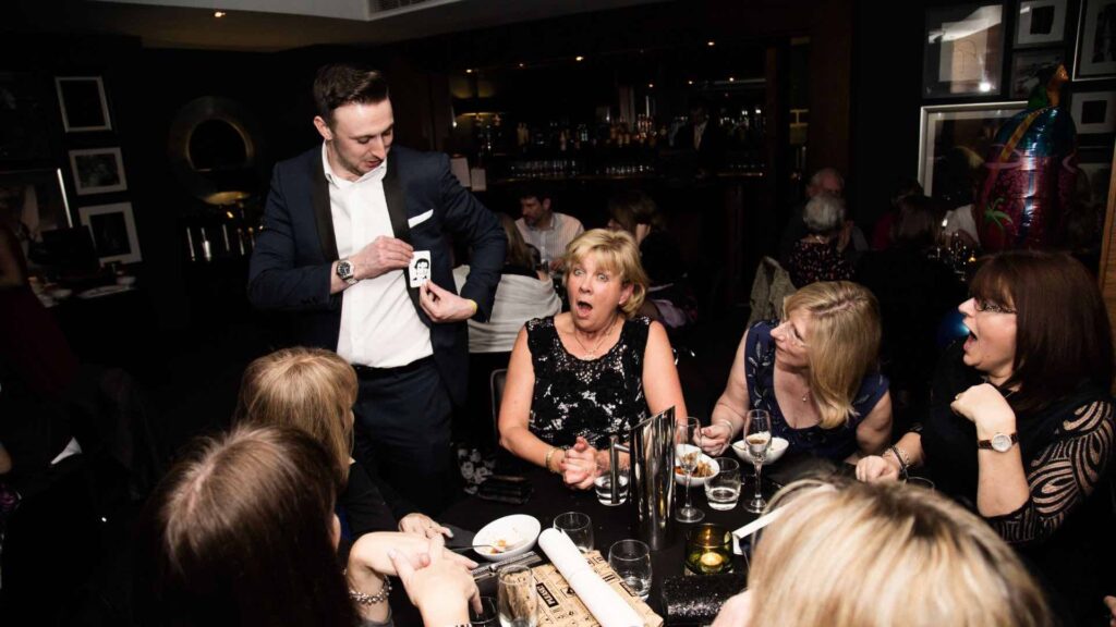 A corporate event magician wows a table of people with a magic trick