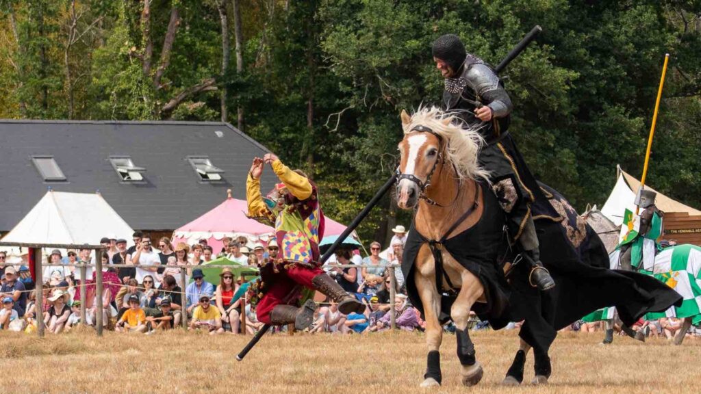 A jester is knocked off his feet by a jousting knight