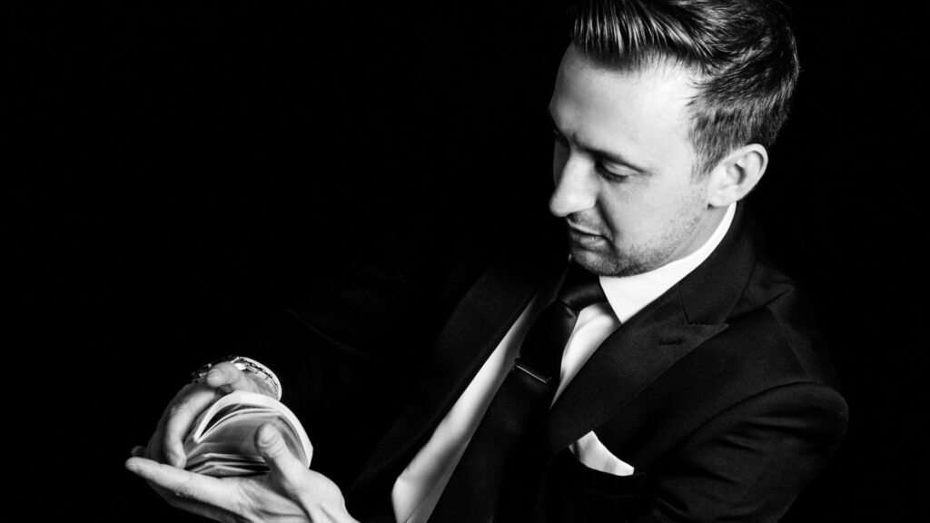 A magician poses in black and white for a portrait shot with a deck of cards