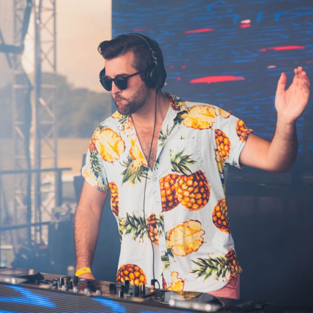 A club party DJ raises his hand to crowds while mixing