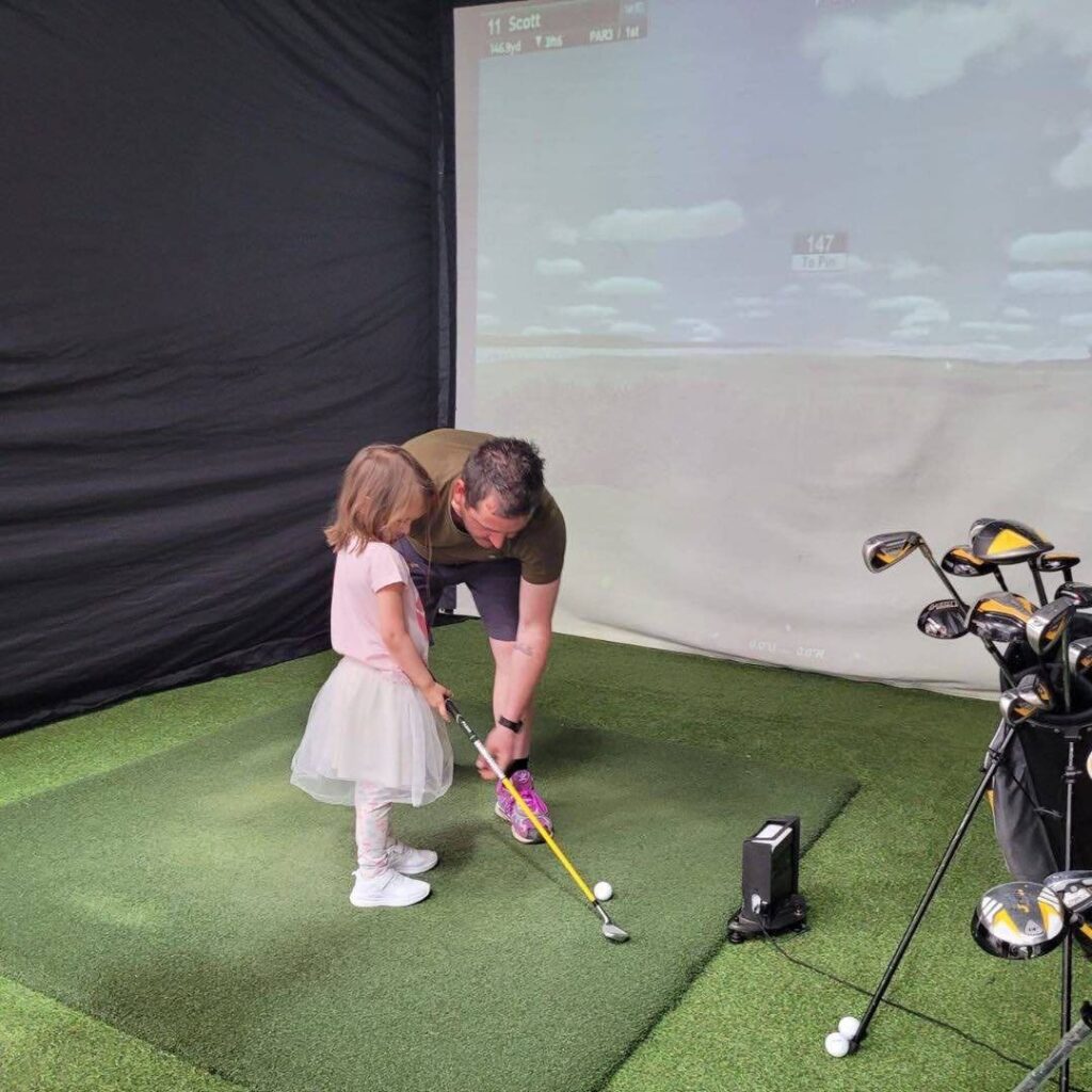 Man showing child how to use golfing simulator at event