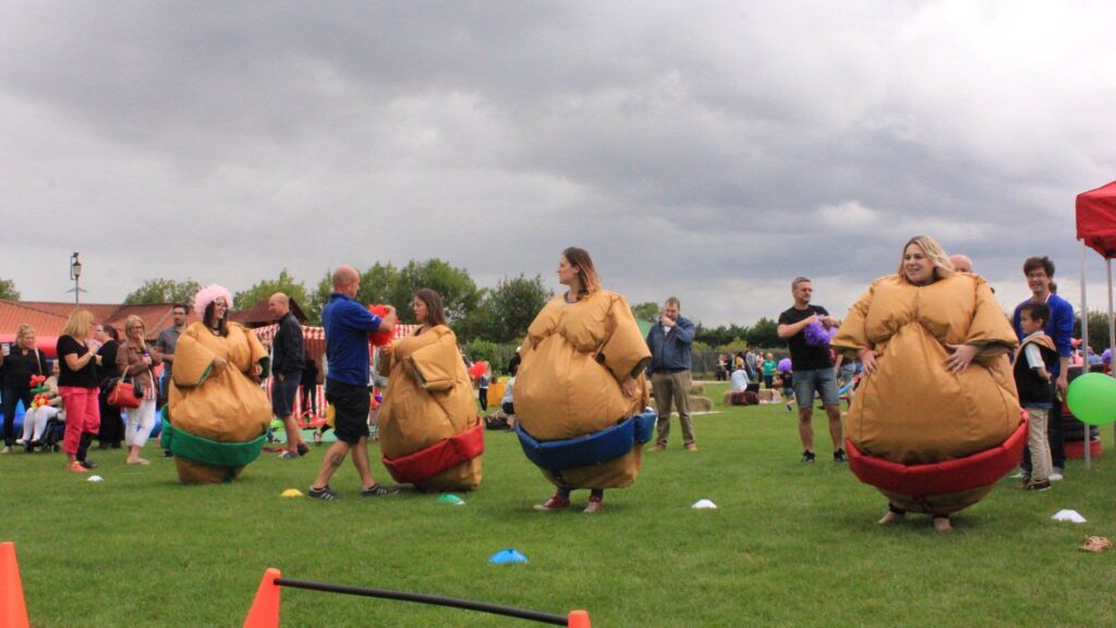 Guests wearing sumo wrestling suits lined up on green at company fun day and preparing to take part in a team building race.