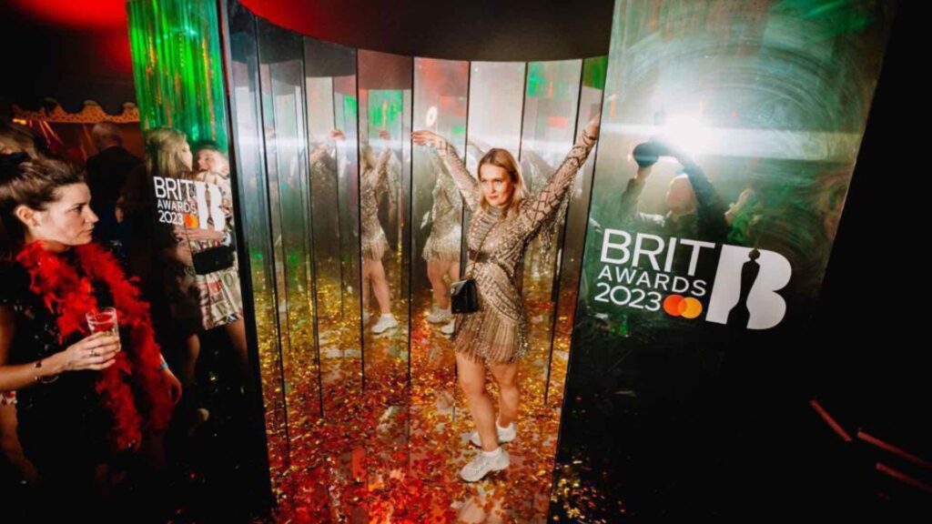 A lady poses inside a photo booth surrounded by segmented mirrors.