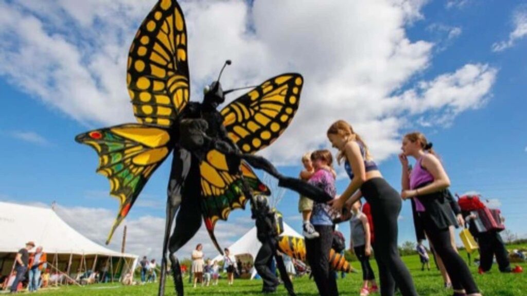 A butterfly stilt walker interacting with three children