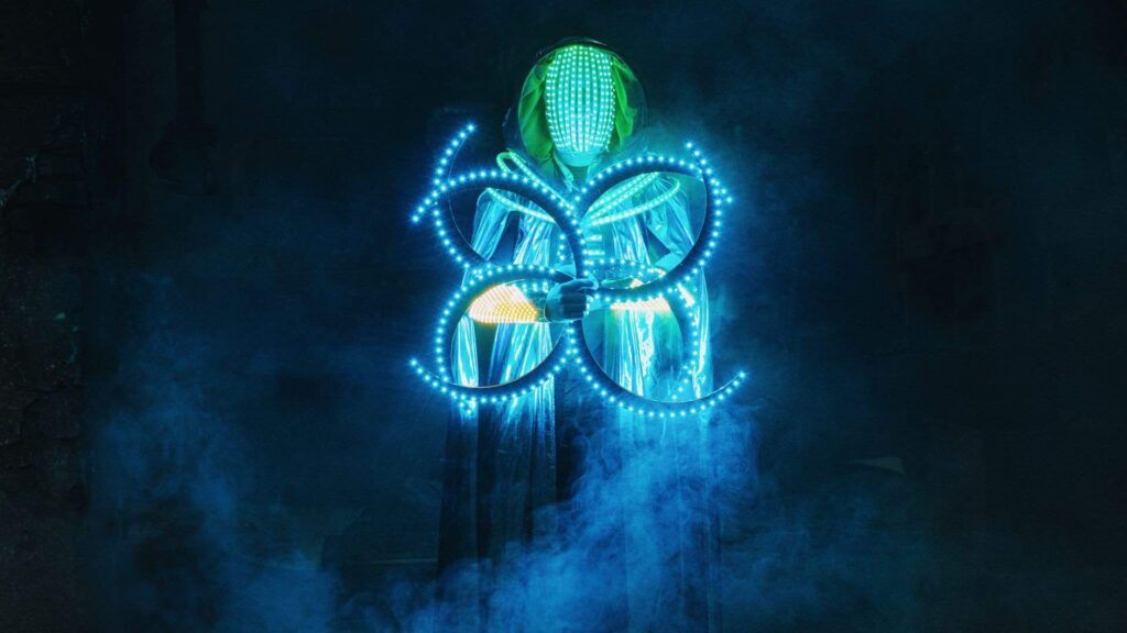 An LED dancer stands on stage with a blue glowing symbol