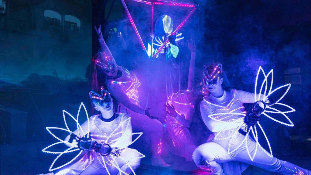 A purple lit stage features LED dancers posing with glow sticks