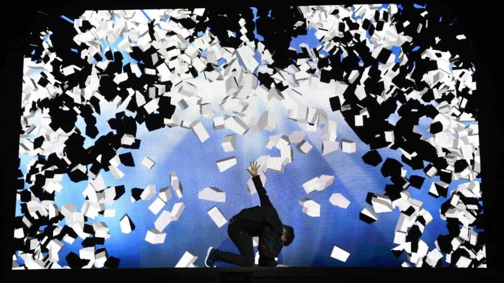 An urban dancer kneels on the floor infront of LED cubes projection