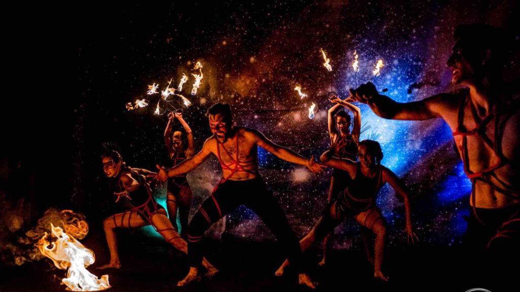 A troupe of fire performers hold flamed in their hands while dancing