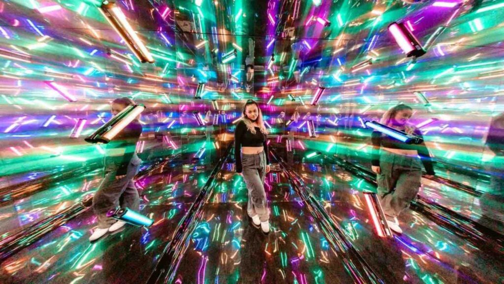 A girl stand amongst LED lights inside an immersive mirror photo booth