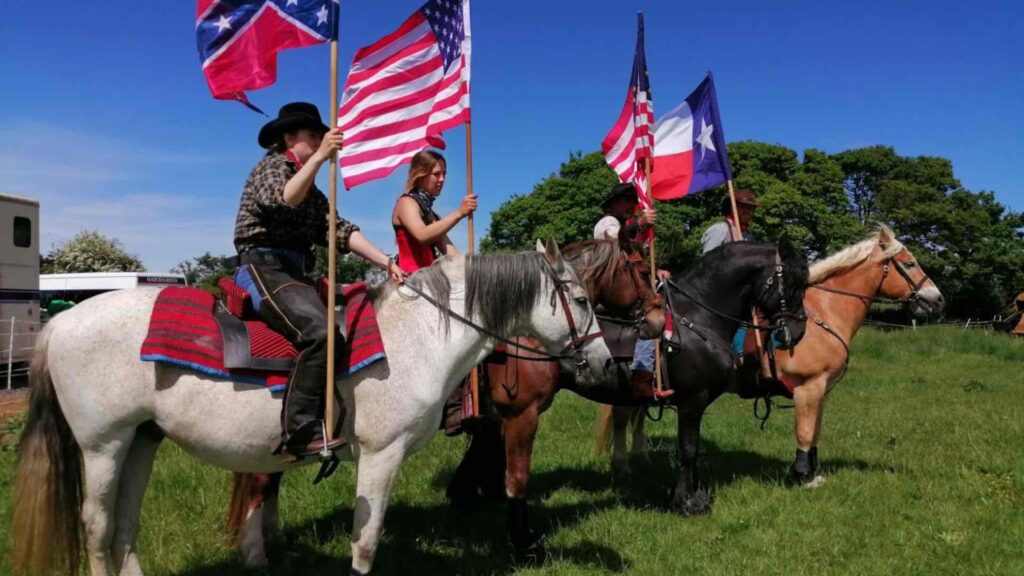 Horse and cowboy riders holding american flags in a field
