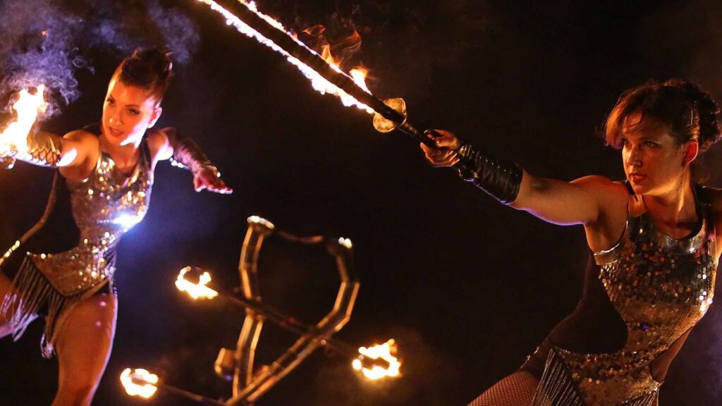 Two fire performers use flaming weapons during an artistic fire show