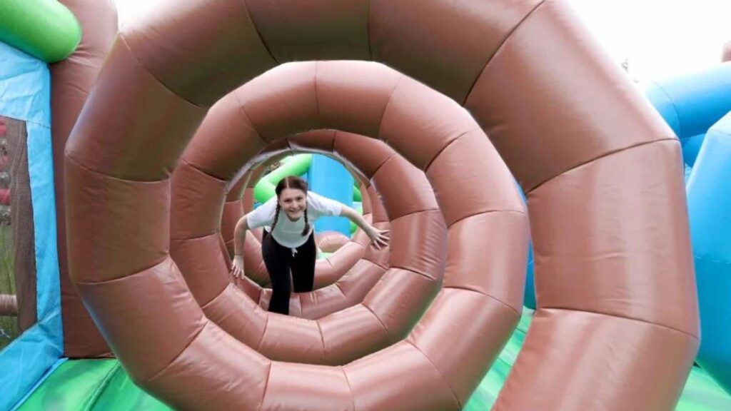 A girl crawls through a brown spiral inflatable course