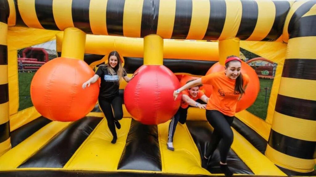 Yellow and black inflatable obstacle course with red balls and participants.