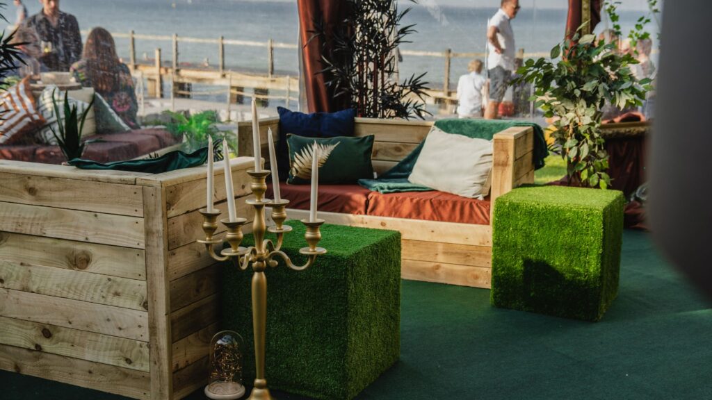 Two pallet sofas decorated with green and copper cushions inside marquee.