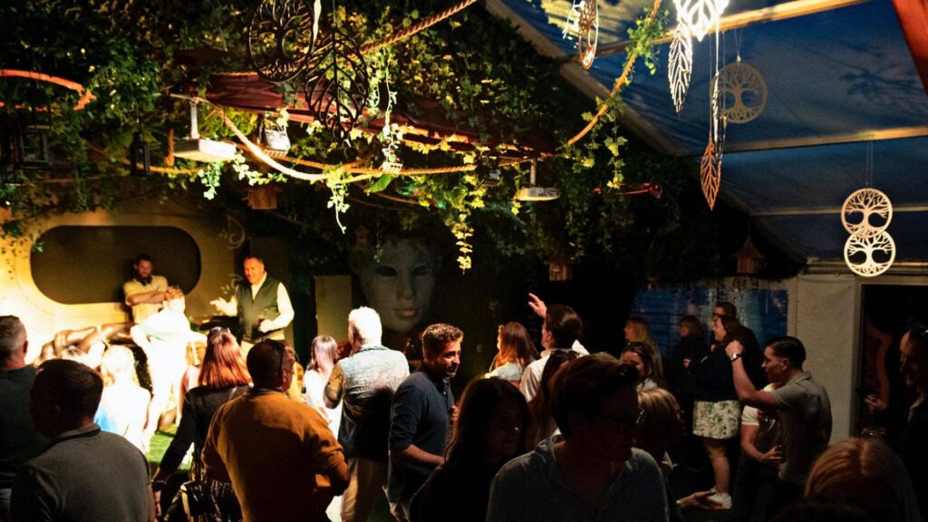 Adults enjoying the evening in a marquee with dangling garden theme foliage and set design