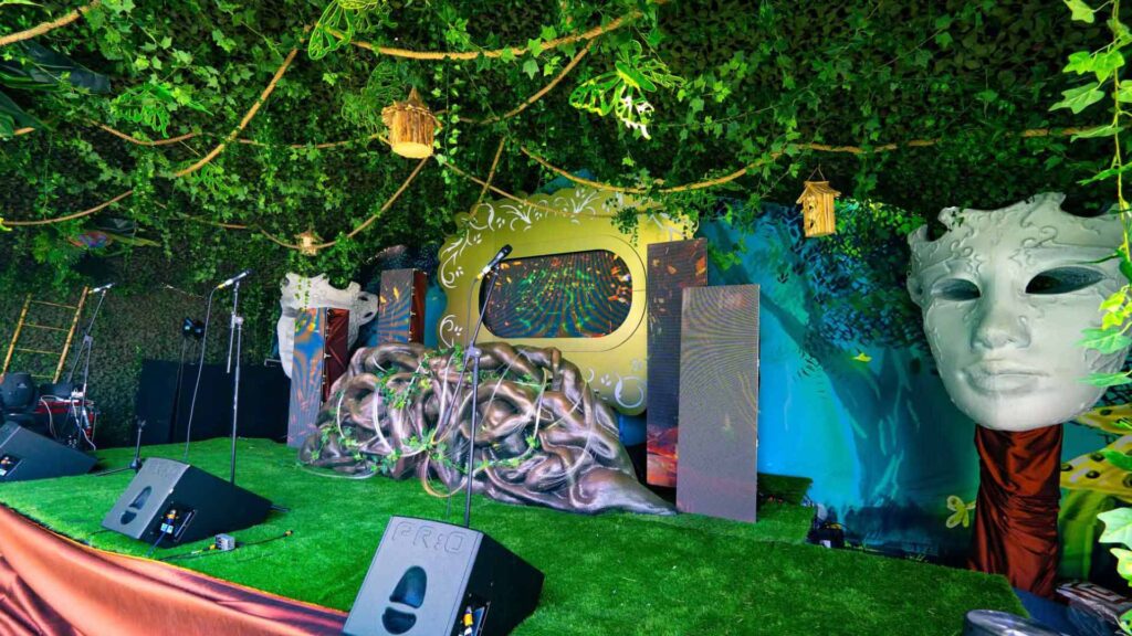 A stage set design featuring enchanted garden theme props such as foliage and hanging ornaments with an inbuilt 3D projection