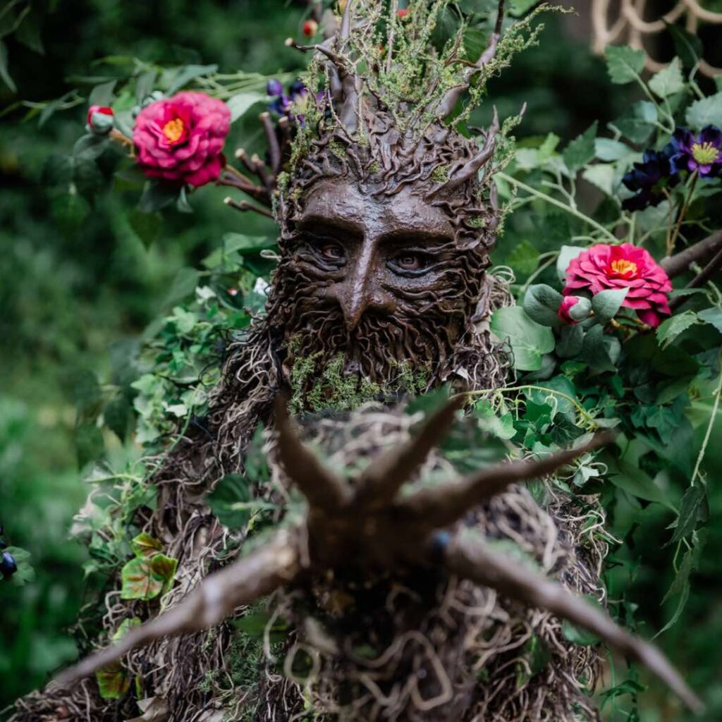 A forest themed stilt performer reaches his branch hand to audience