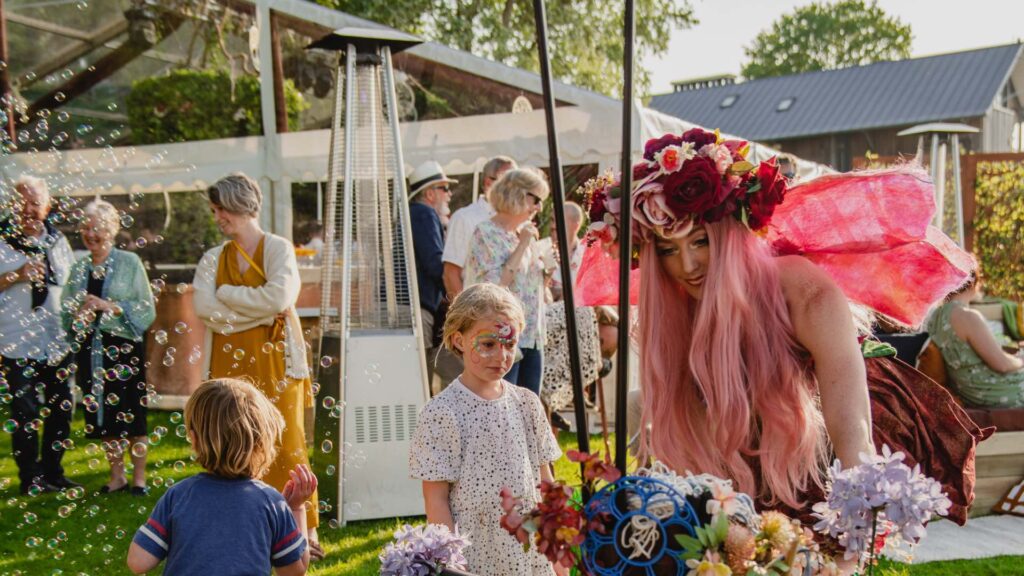 A spring themed fairy dressed in rose costume blows bubble with children for entertainment alongside her cart of flowers