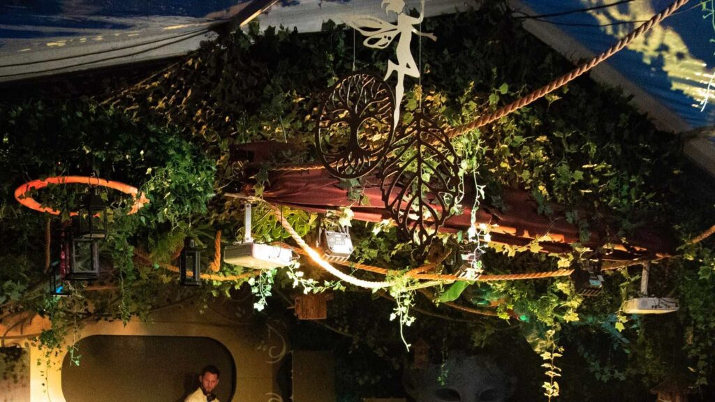 A ceiling shot of an enchanted forest theme party featuring lights, beams and foliage