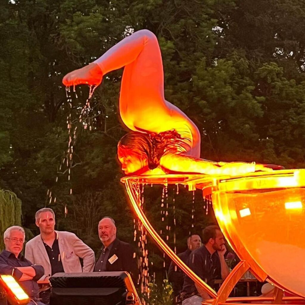 A water bowl contortionist performs on a large water apparatus for audiences