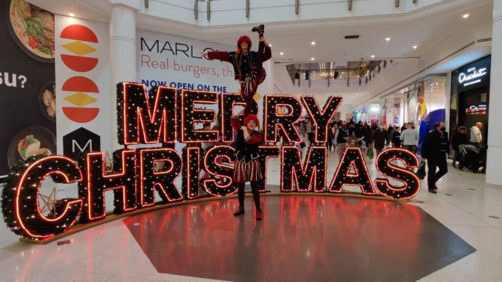 A duo of christmas elves perform daring acrobat in shopping centre