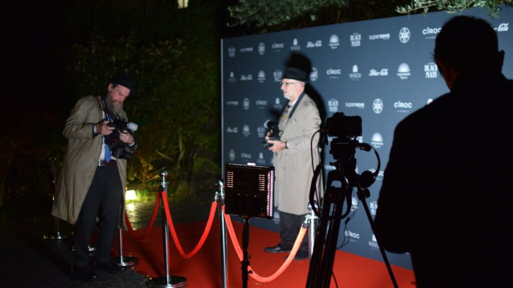 Red-carpet area with fake paparazzi and branded photo backdrop used at front of Halloween mansion party.