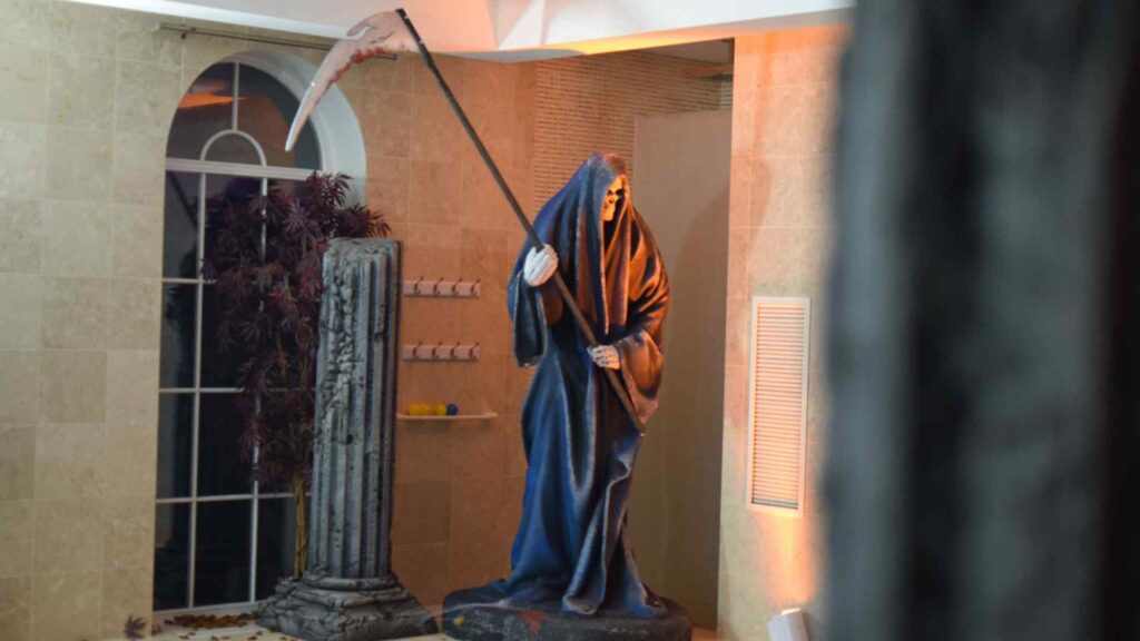Large grim reaper prop placed next to swimming pool at Halloween mansion party.