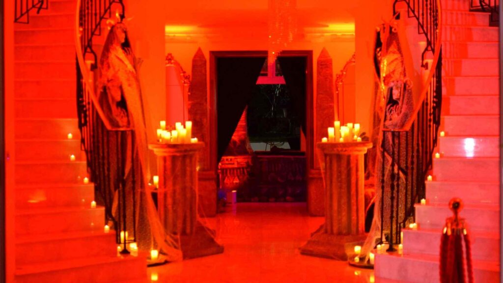 Hallway / entrance of Halloween mansion party with spiral staircases, statues and candles, complete with red projection lighting.