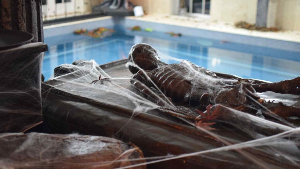 Bespoke cobwebbed black skeleton prop used to decorate pool area of Halloween mansion party.