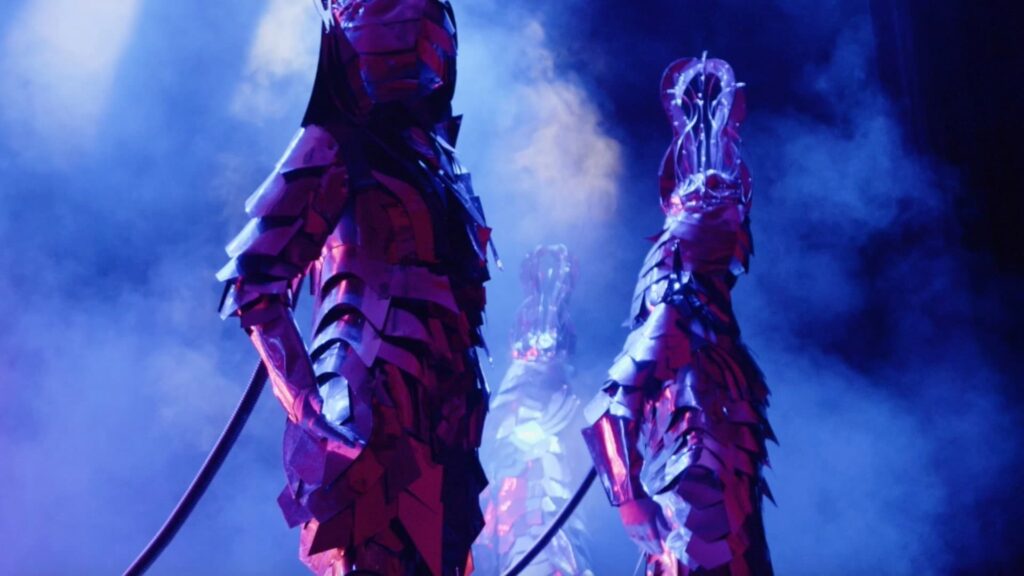 Three mirror-costumed dancers performing on stage under LED lighting.