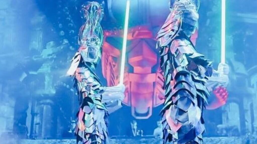 Mirror-costumed dancers holding glowing swords on a dark stage.