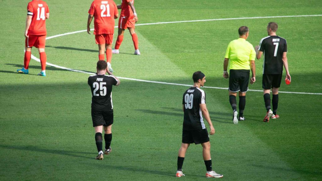 Half time whistle blown, players applauding, beginning to walk off of pitch.