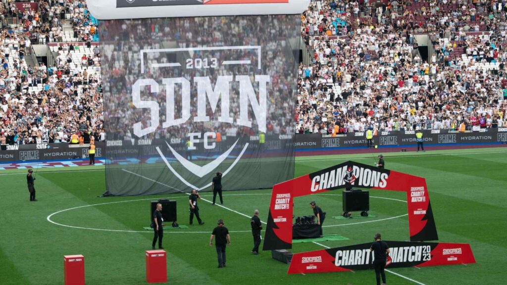 Production team hanging Sidemen FC banner and setting up awards facade for trophy lift.