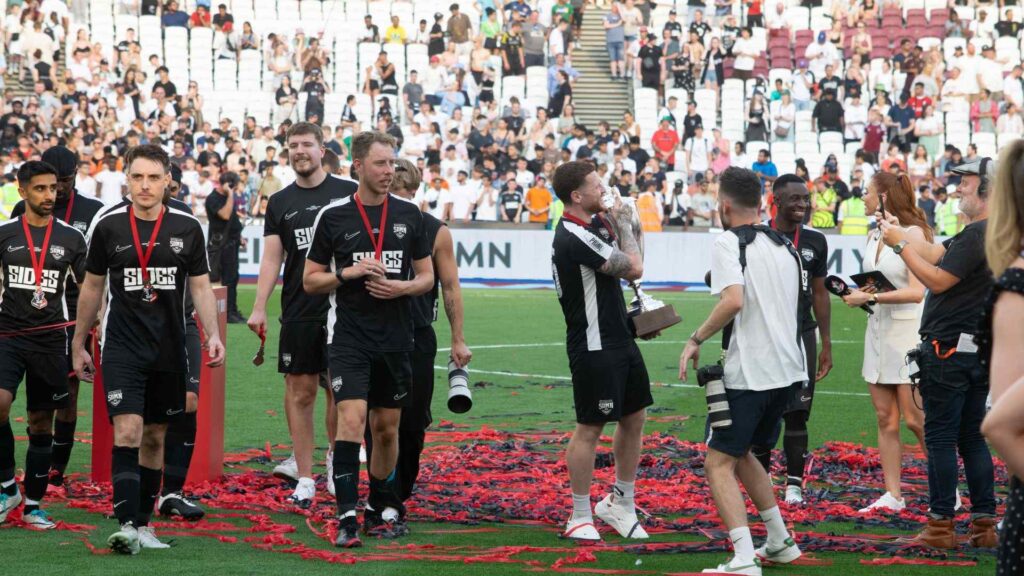 Sidemen FC parading winners trophy on pitch.