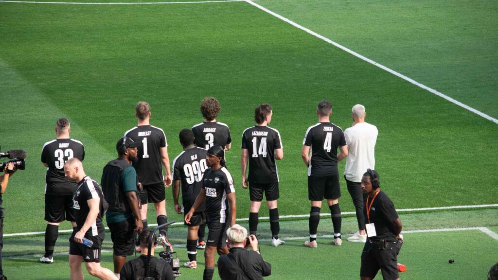 Sidemen FC substitutes standing pitch side, watching the game.