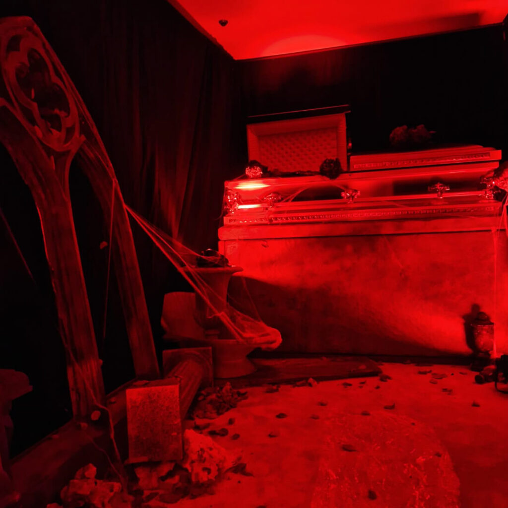 A coffin and props highlighted in blood red lighting for cult horror theme.