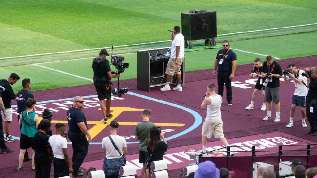 Aitch walking through player tunnel on to pitch with camera man filming from the front for the livestream.