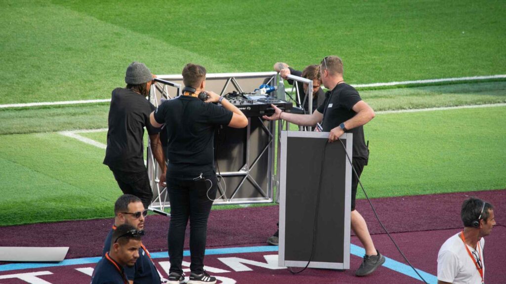 Production team setting up Aitch's DJ's equipment and desk for halftime performance.