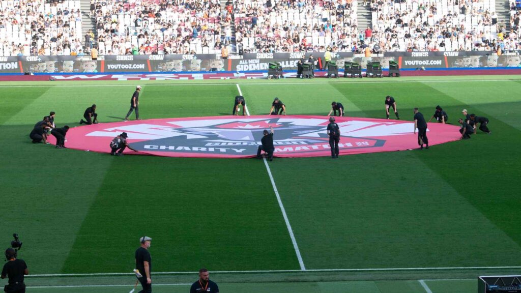 Cadets and volunteers led by production team setting up centre circle for Aitch's halftime performance on the pitch.