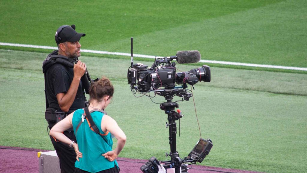 Standing livestream camera, pitch side, operated by camera man and assistant.