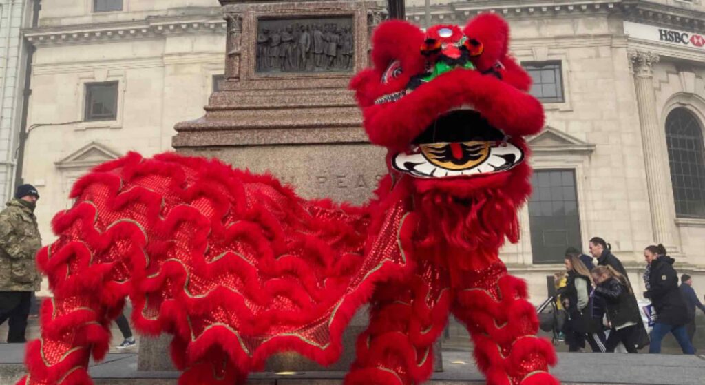 Red Chinese lion walkabout performer at a public event outside a London monument.