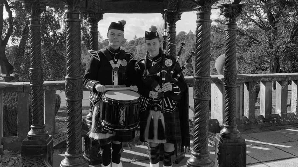 Bagpiper and drum duo stood under bandstand at public event.