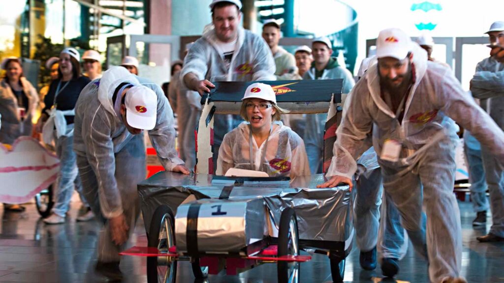 Lady being pushed in F1 go kart built by employees for team building event.