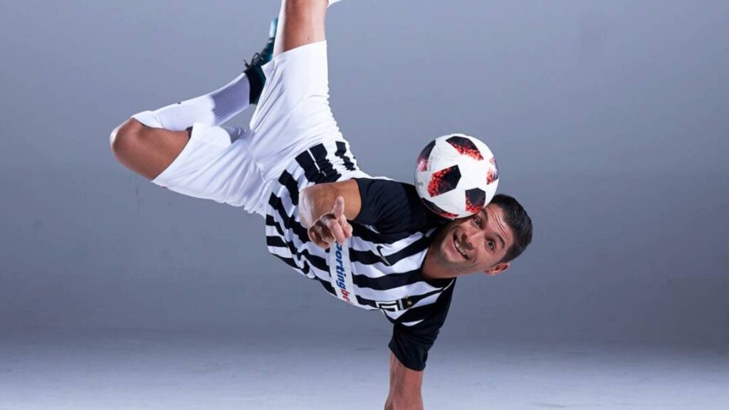 Cristiano Ronaldo lookalike football freestyler performing trick handstand in black and white stripes.