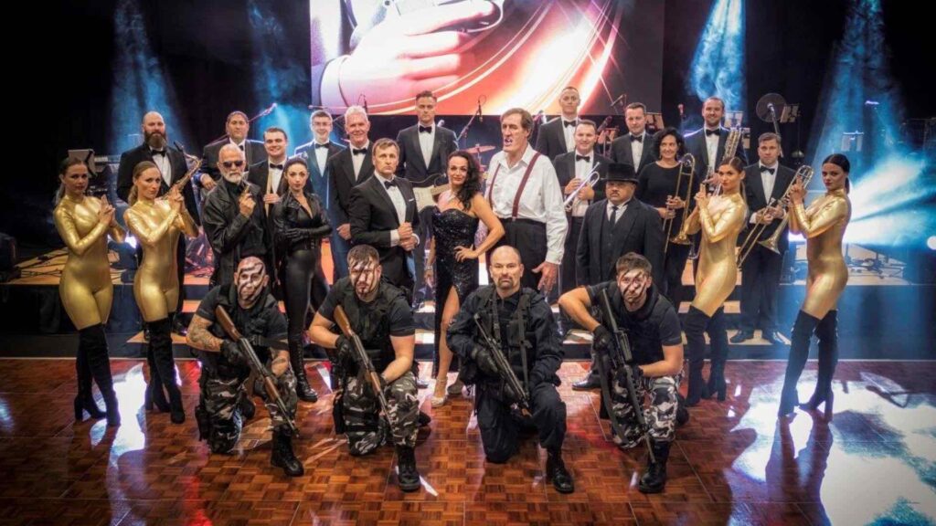 James Bond stunt performers alongside tribute band on stage at a gala dinner.