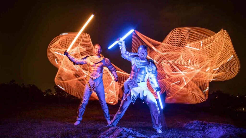 LED performers for sports events with light up props and orange light patterns in gladiator costumes.