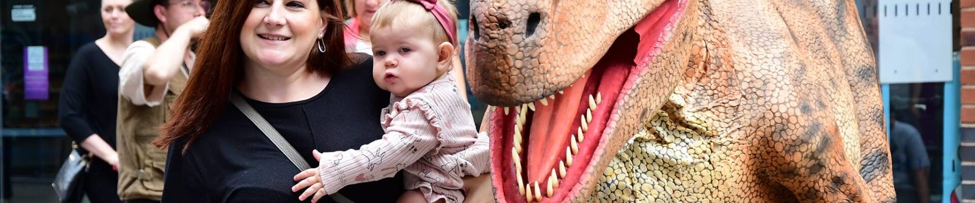 Walkabout dinosaur with baby and mother at a public event.
