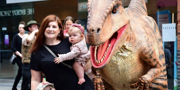 Walkabout dinosaur with baby and mother at a public event.
